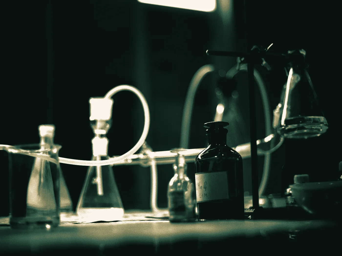 Baloane Erlenmeyer si o sticla de reactiv pe o masa de laborator slab luminata